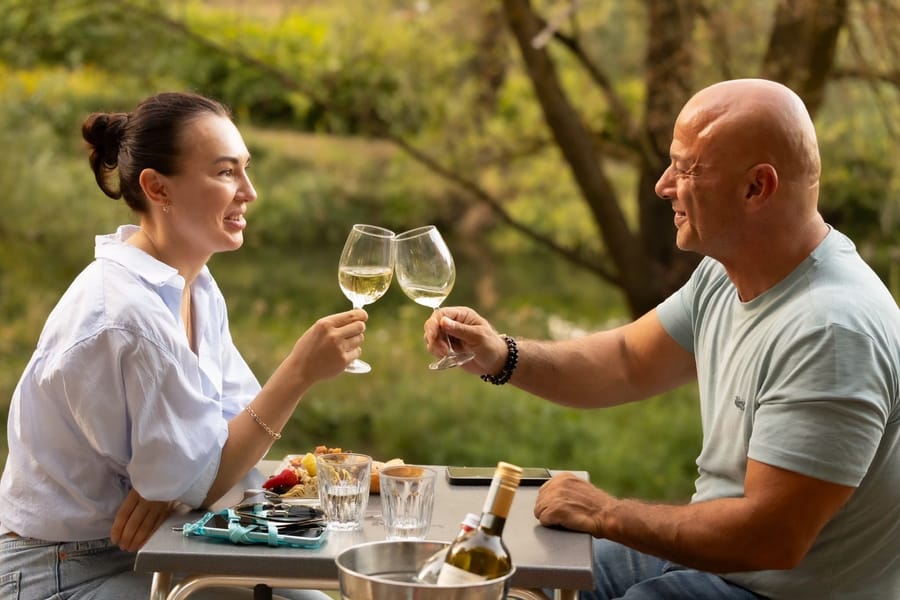 Ein Paar stößt mit Weißwein an einem gedeckten Tisch im Grünen an
