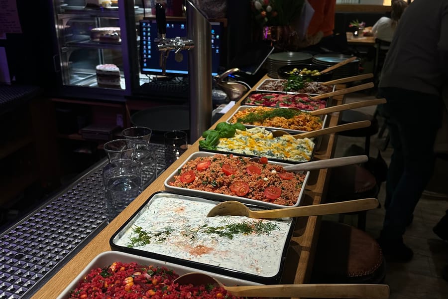 Buffet am Tresen mit Kısır, Joghurtdip und weiteren Schalen, im Hintergrund Gäste