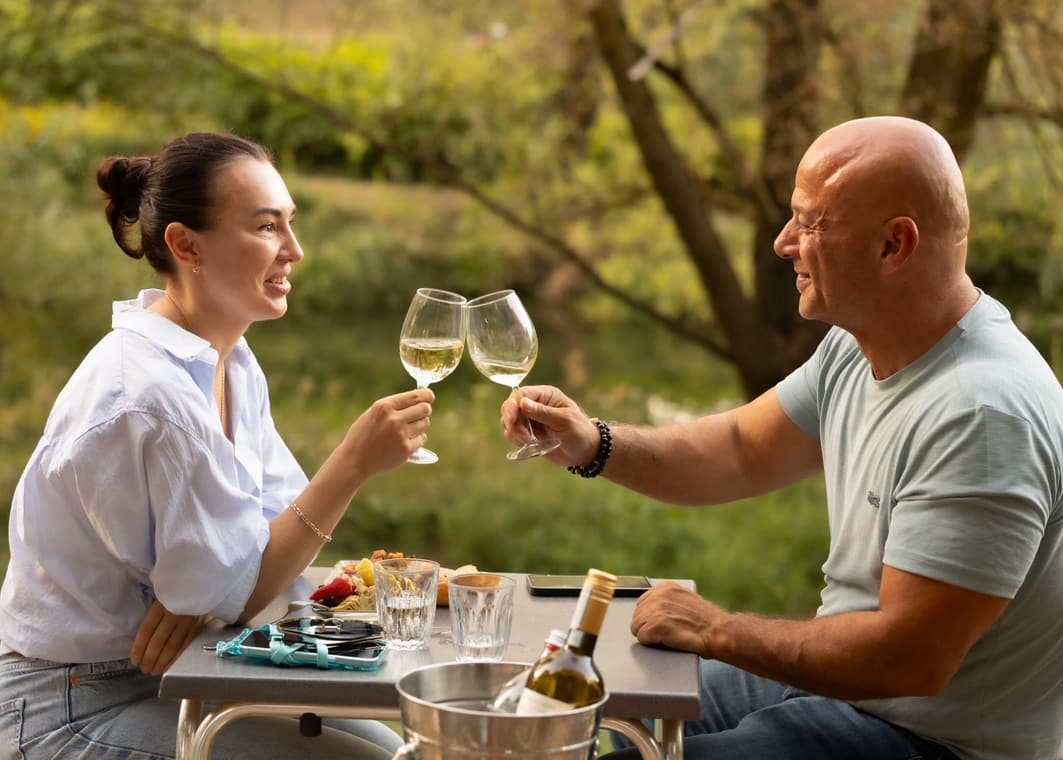 Ein Paar stößt mit Weißwein an einem Tisch im Grünen an