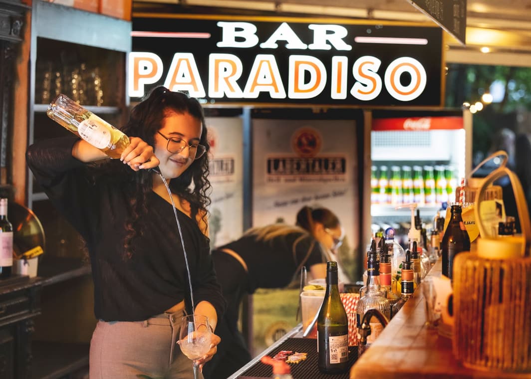 An der Bar Paradiso wird ein Aperitif eingeschenkt, darüber das Leuchtschild