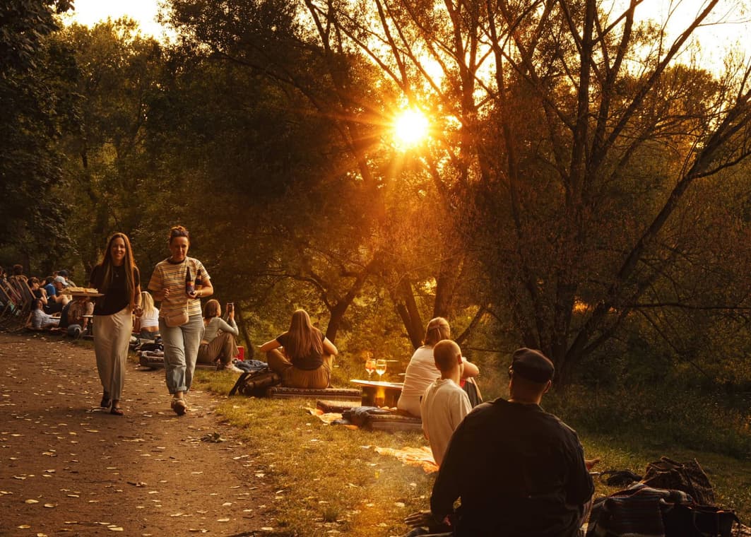 Gäste im Abendlicht am Grieser Spitz, jemand bringt ein Tablett, Sonne durch die Bäume