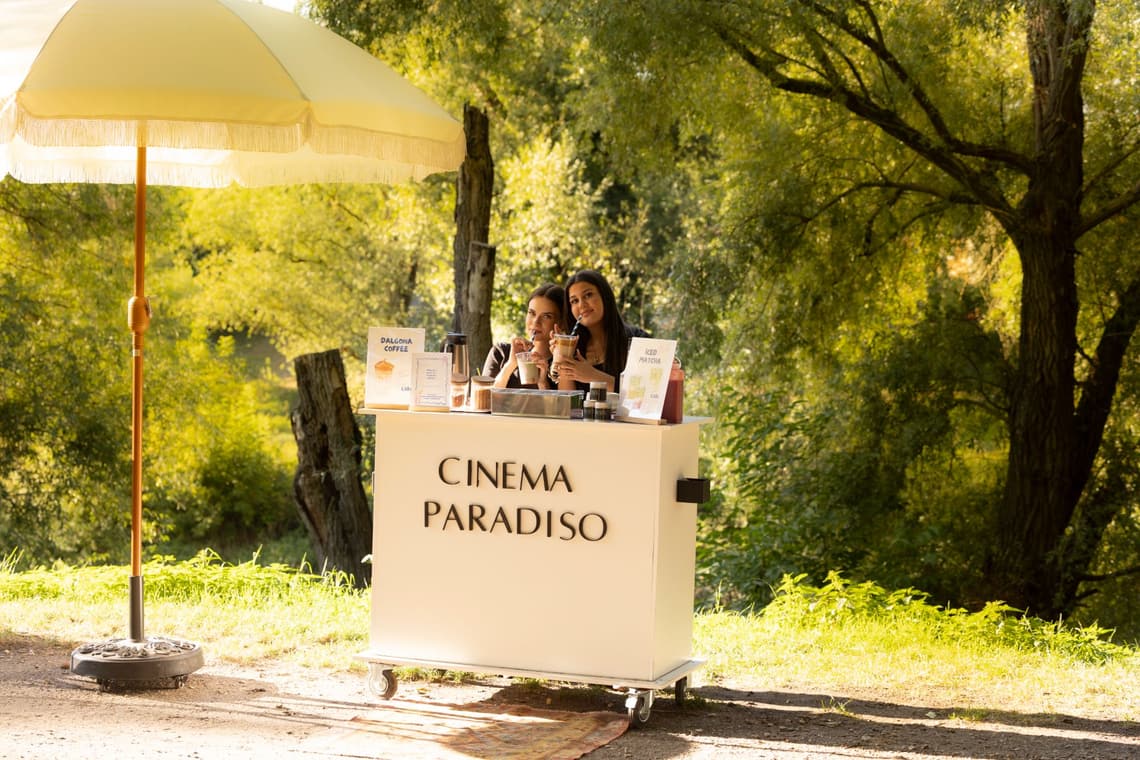 Zwei Frauen am cremefarbenen Cinema-Paradiso-Wagen mit gelbem Sonnenschirm